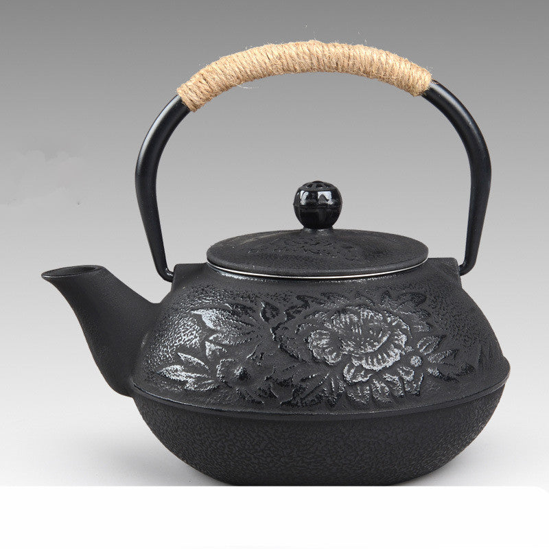 Black cast iron teapot with rose embossing and rattan handle, ideal for brewing tea in a stylish, durable design.