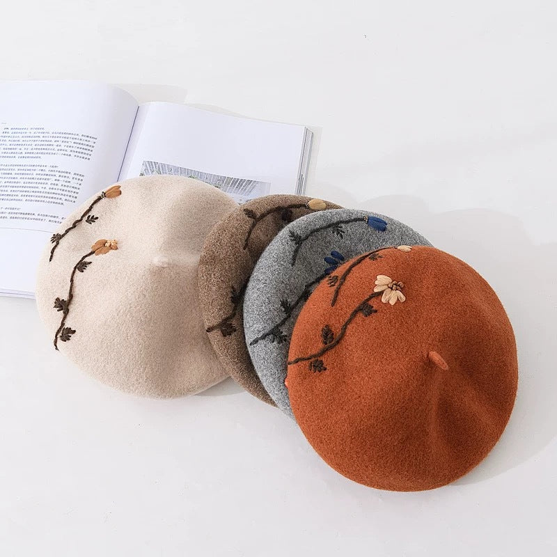 Six embroidered mushroom meadow daisy berets in beige, black, khaki, brick red, camel, and gray with daisy embroidery around the edges.