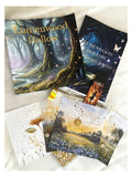 A flat lay of Lumenwood Hollow themed stationery and journaling supplies on a white fabric background, including a forest illustration book, a journal, a jar candle, and several decorative cards and paper pieces.