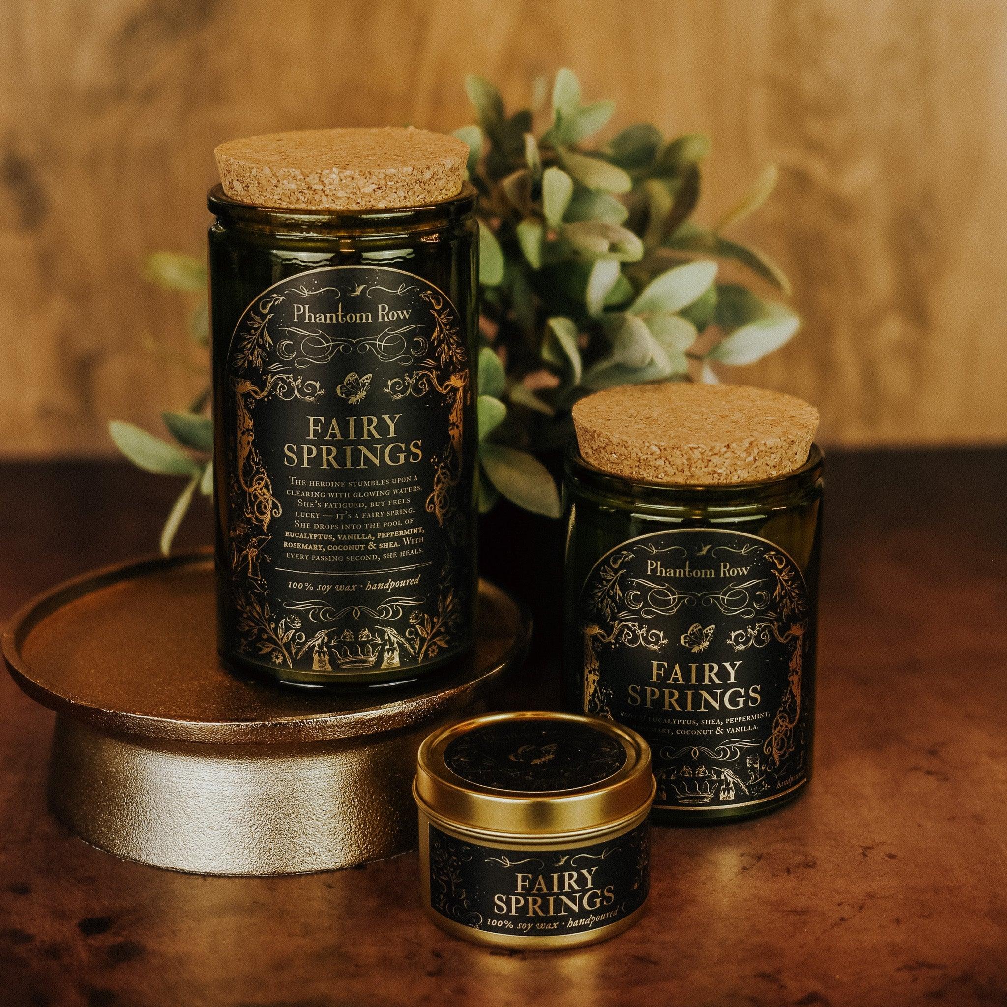 Phantom Row Fairy Springs Candle with whimsical fairy family design, set against a soft, glowing background.