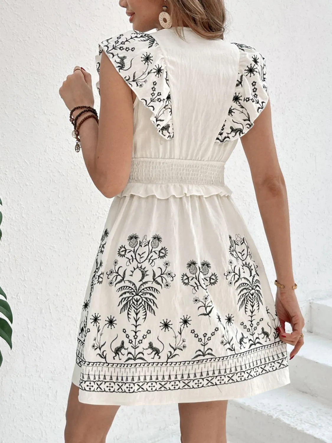 Back view of a cream Woodland Muse smocked mini dress by Trendsi, featuring a fitted bodice and short puff sleeves on a model.